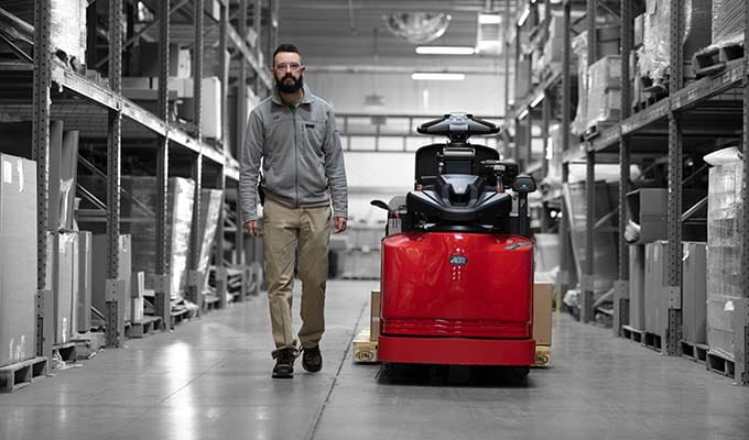 Black and white view of inside of warehouse of a man next to a red Raymonds vehicle.